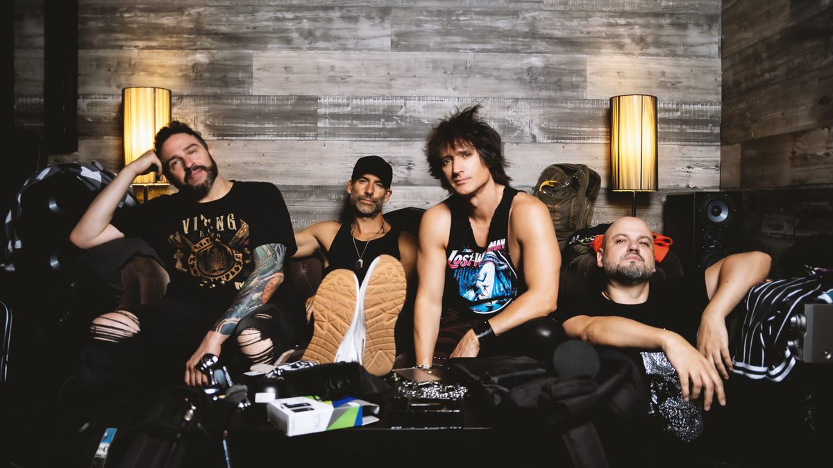 The four members of Lost Wingman sitting on a couch in their rehearsal room, among amps and lit lamps